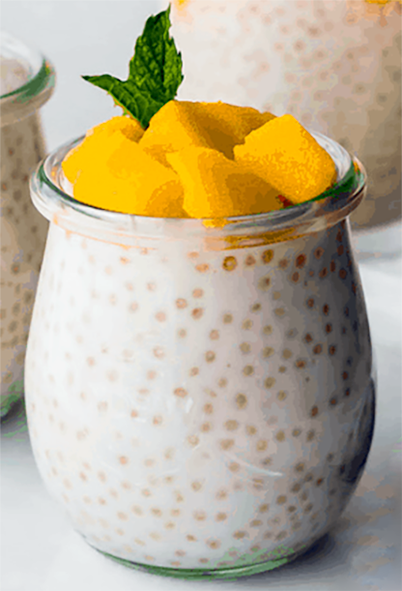 pomelo sago pudding in a glass yoghurt pot topped with mango and a sprig of mint