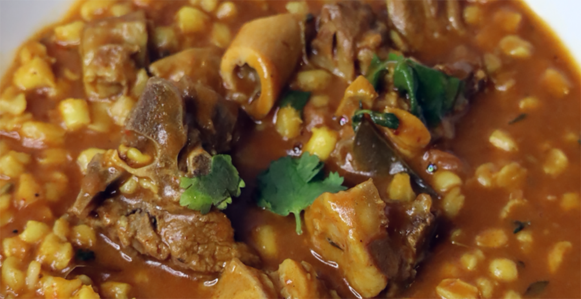 stew of goat meat, samp and beans in a tomato and onion base with chillies in a bowl