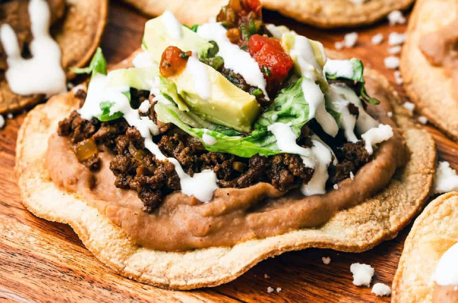 assembled beef tostada on a wooden chopping board