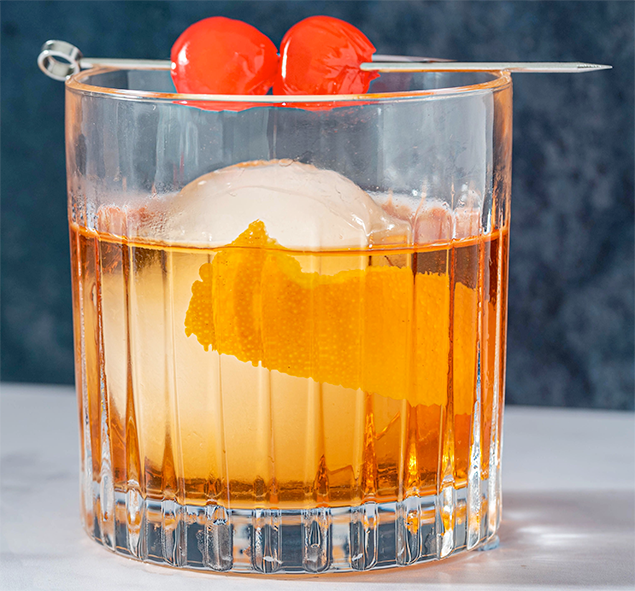 whisky-based old fashioned cocktail in a rocks glass with ice, lemon peel and maraschino cherry garnish