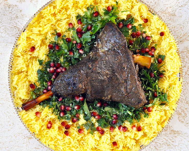 shuwa, omani spiced leg of lamb served over flat-leaf parsley and pomegranate arils on a bed of saffron rice