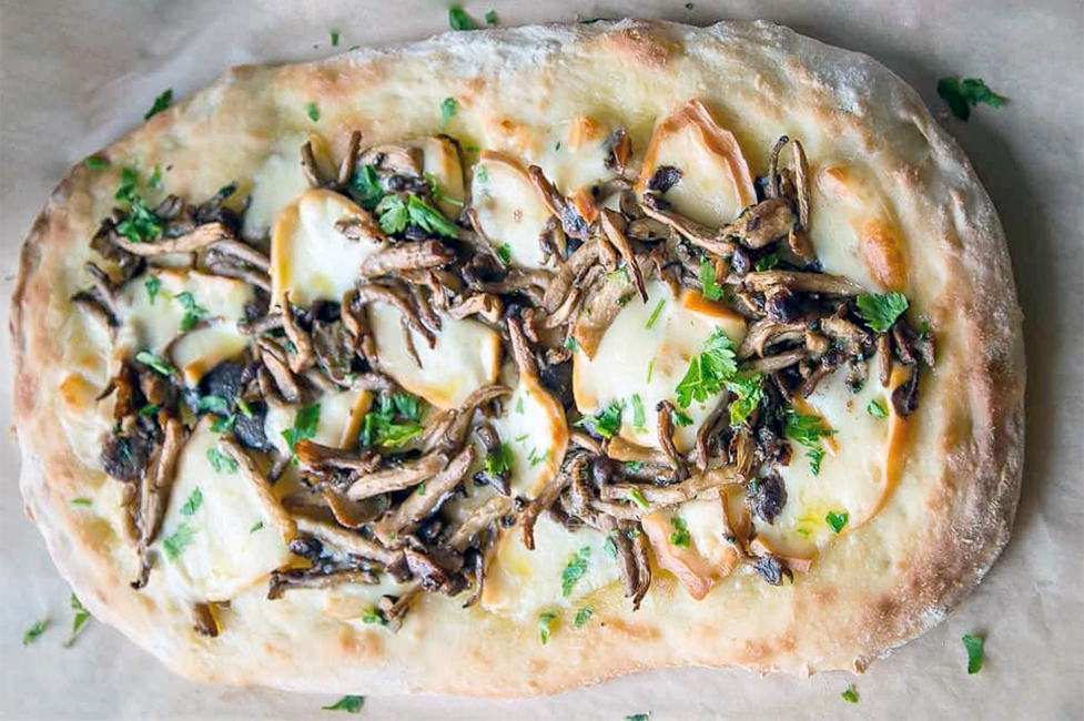 oval pinsa romana pizza on a marble work top with mushroom and provaone cheese topping