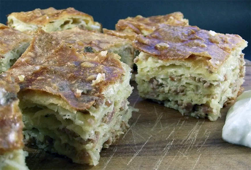 sheets of filo pastry with a meat filling cut into squares and arranged on a chopping board