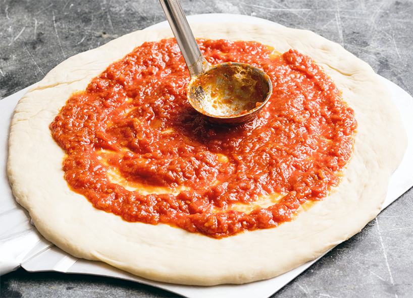 Home made pizza sauce ladled and spread onto a fresh pizza base