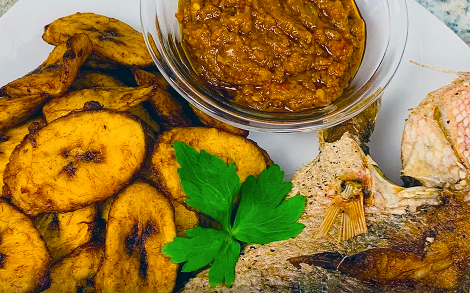 fried fish and fried plantains served on a plate with red oil in a glass bowl