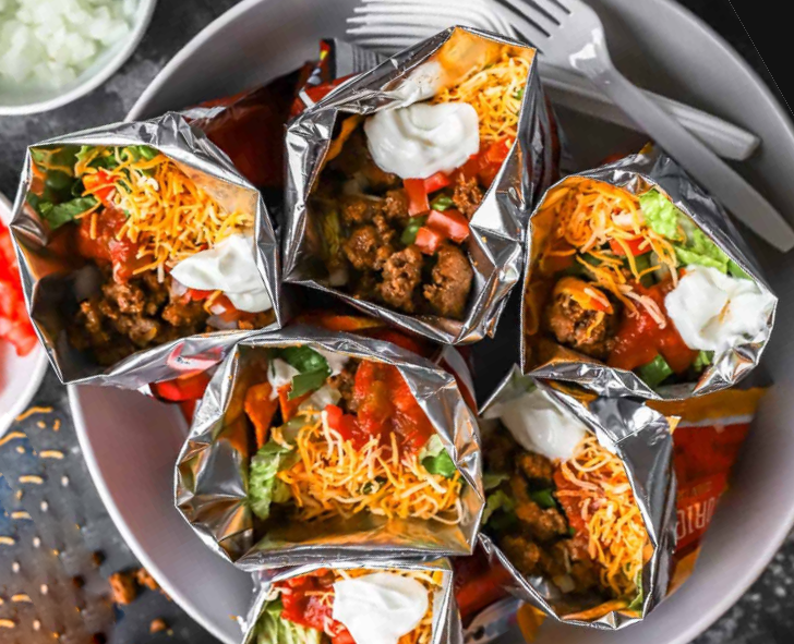bags of corn chips topped with beef, tomatoes, lettuce, cheese, salsa and sour cream making portable tacos