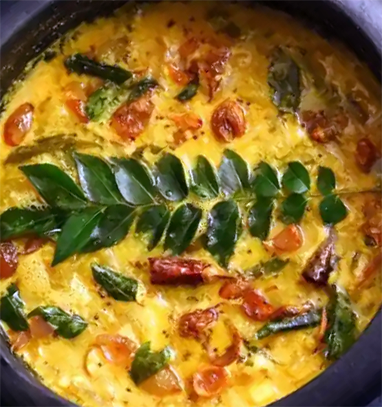 raw mango and jackfruit seed curry garnished with a sprig of curry leaves in a clay pot
