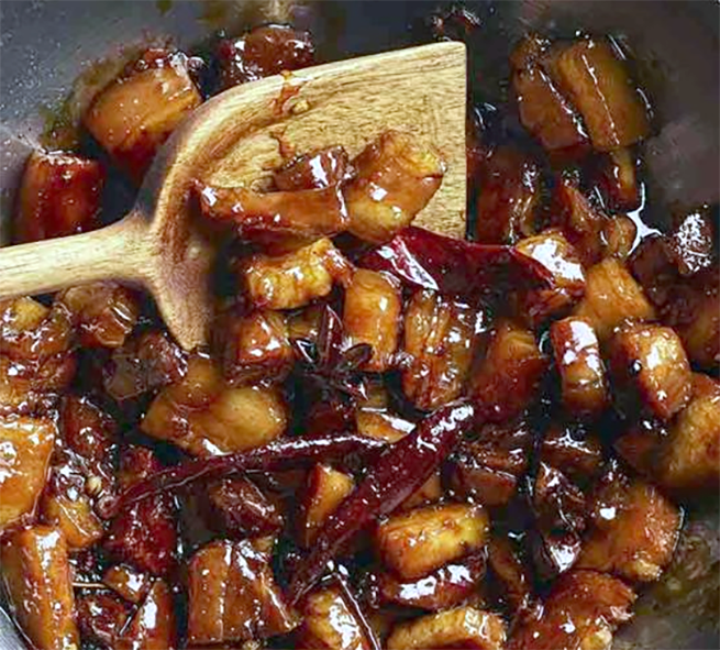 red-braised pork belly being stir-fried in a wok