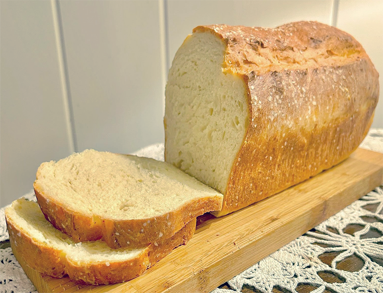 loaf of reedmace pollen bread on a wooden cutting board with two slices cut