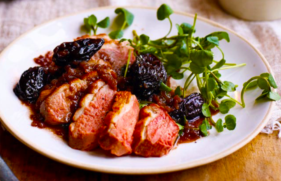 sliced duck breasts with prunes and watercress on a white plate