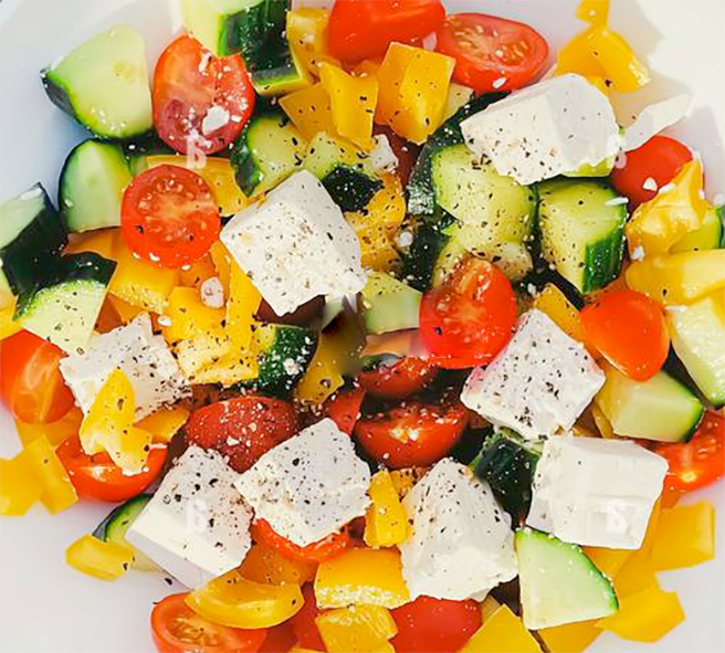 Greek salad of cubed bell pepper, tomatoes, cucumber, celery and Feta cheese on a white plate