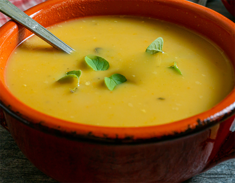 yellow split pea soup in an earthenware bowl garnished with fresh baby oregano leaves
