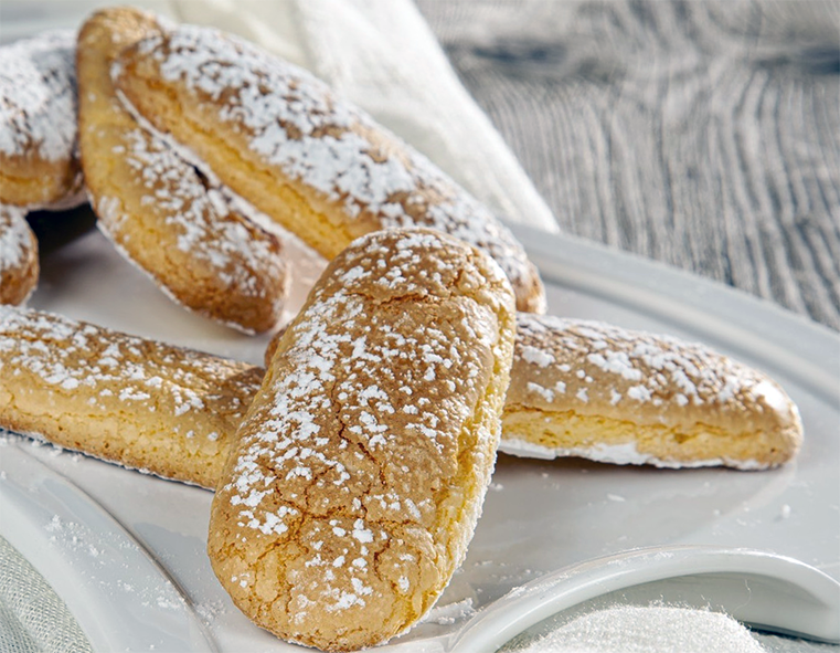 Savoiardi biscuits dusted with icing sugar arranged on a plate
