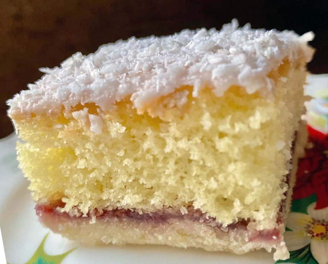 Square section of Scottish snow cake showing the pastry base, jam filling with the sponge topping and icing dusted with grated coconut