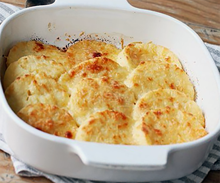 overlapping rounds of semolina gnocchi topped with melted butter and cheese in a white baking dish