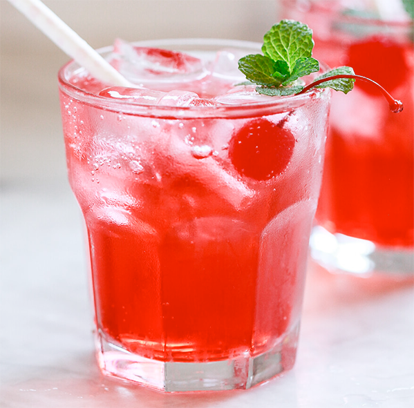 Shirley Temple cocktail in a rocks glass with ice, a maraschino cherry, sprig of mint and a straw