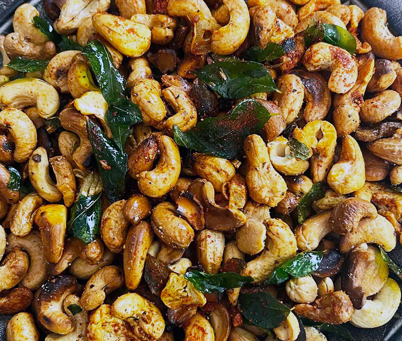Spicy Sri Lankan Fried Cashews served on a plate with fried curry leaves to garnish