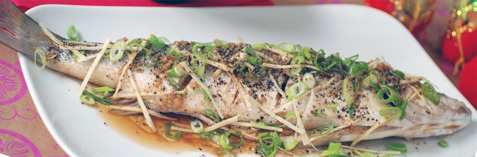 Whole fish served on a white plate with a garnish of julienned ginger and spring onions