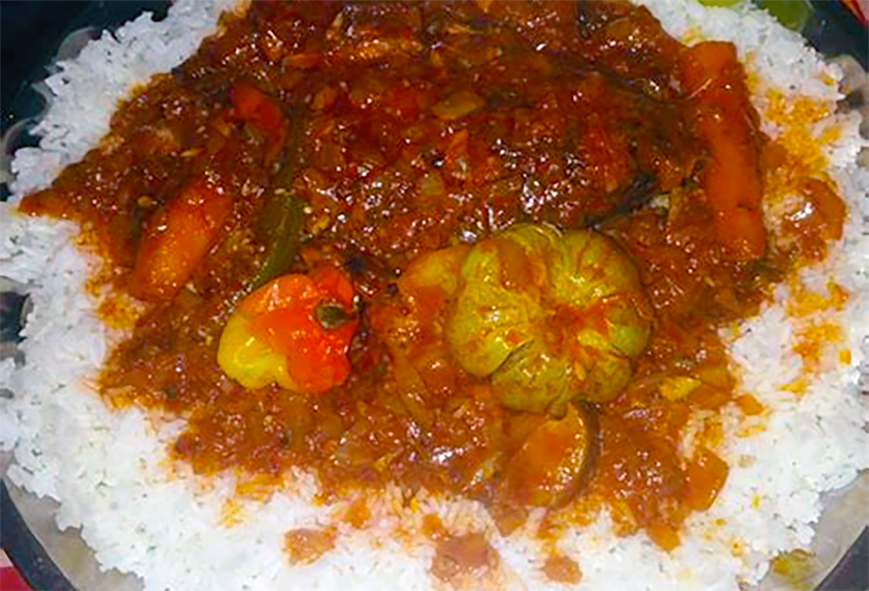 fish in a red palm oil and tomato sauce with vegetables served on a bed of white rice