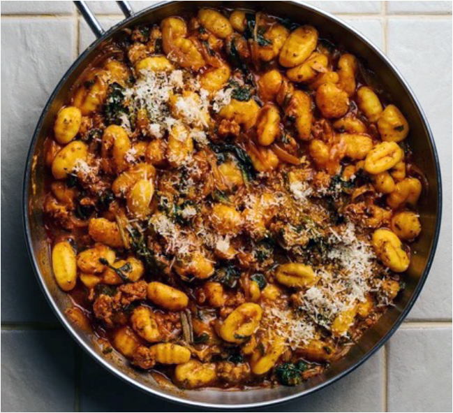 sausage and gnocchi with spinach in a wine and stock base garnished with grated parmesan in a steel frying pan