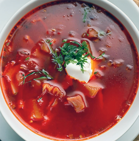 bowl of ukrainian borscht served in a white bowl with a garnish of sour cream and chopped flat-leaf parsely