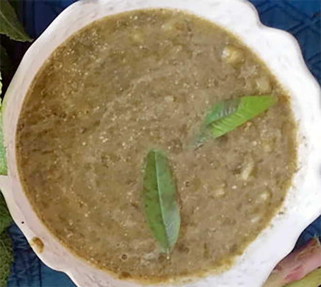 cream of hihiscus leaf soup served in a bowl garnished with two fresh hibiscus leaves