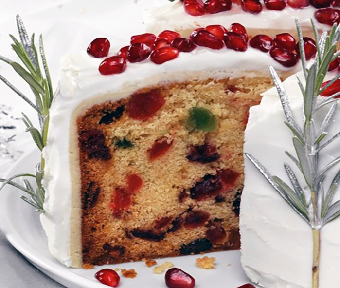 slice of iced white Christmas cake decorated with pomegranate seeds and rosemary sprigs