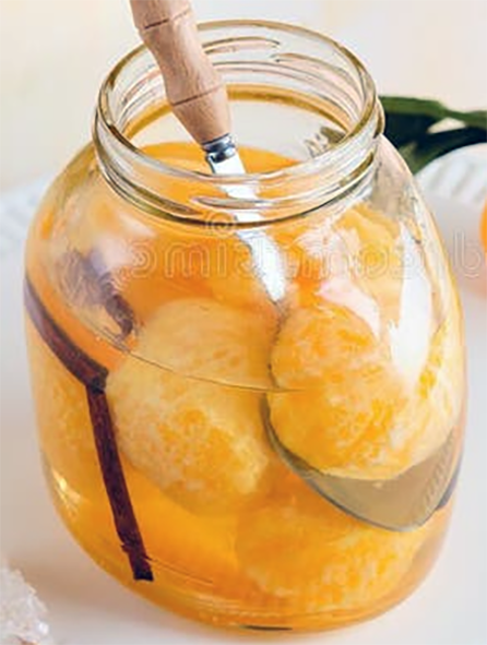 large jar of peeled tangerines in syrup with cinnamon sticks with a spoon lifting one of the tangerines