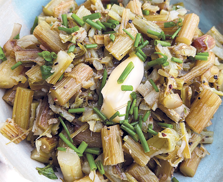 cooked burdock stems piled on a plate and garnished with a pat of butter and snipped chives