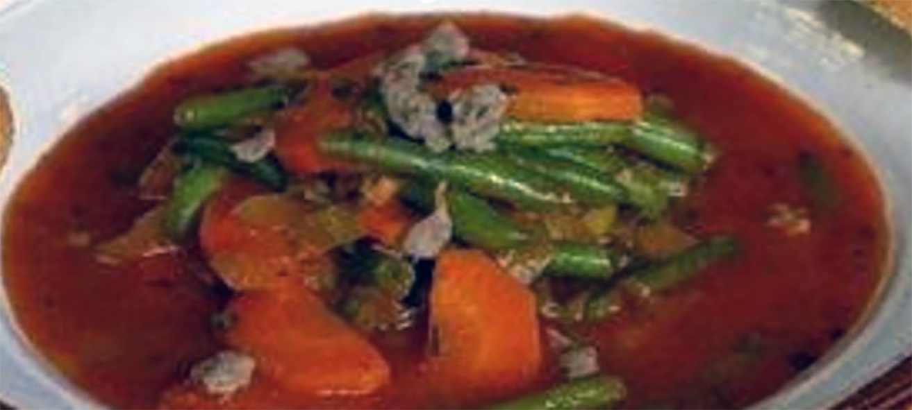 Hungarian green bean soup served garnished with grated cheese in a bowl